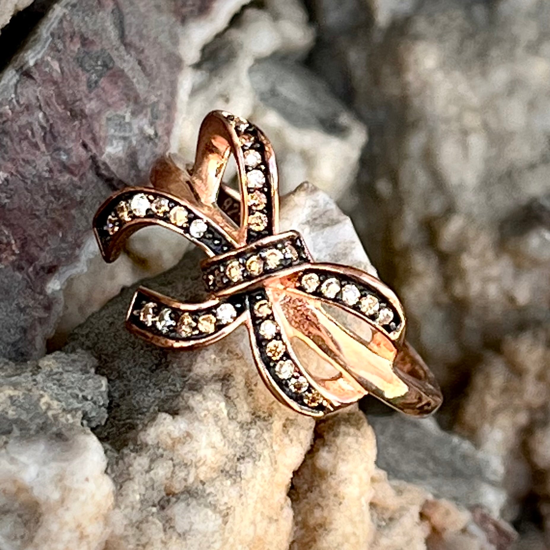 A rose gold colored bow ring.  The bow is tied in a knot, and the knot is set with cognac cubic zirconia.