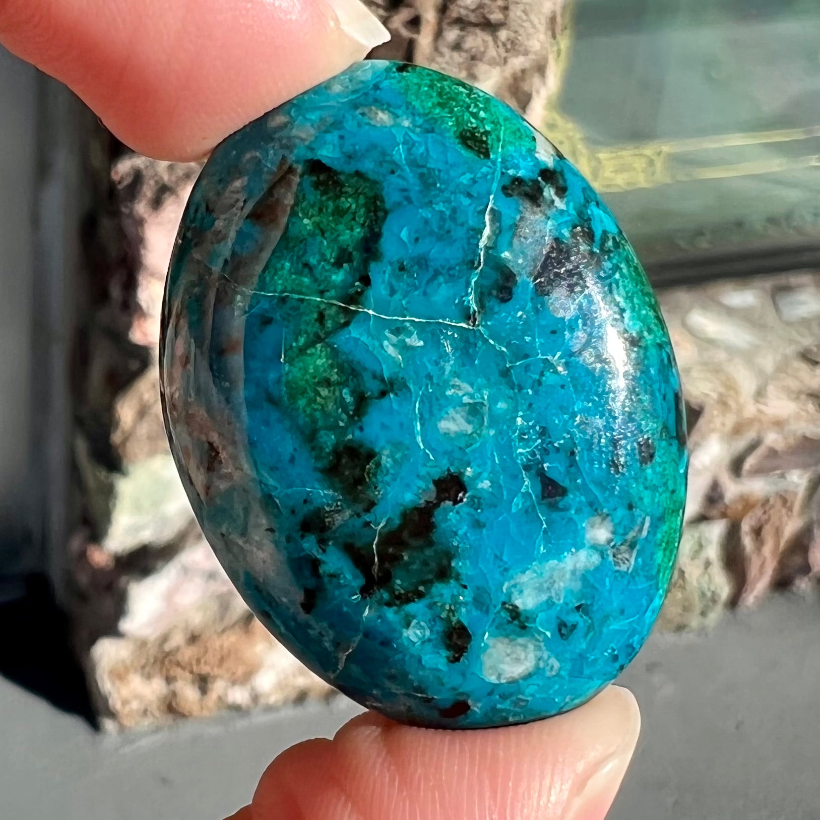 An oval cabochon cut blue chrysocolla with green malachite inclusions.