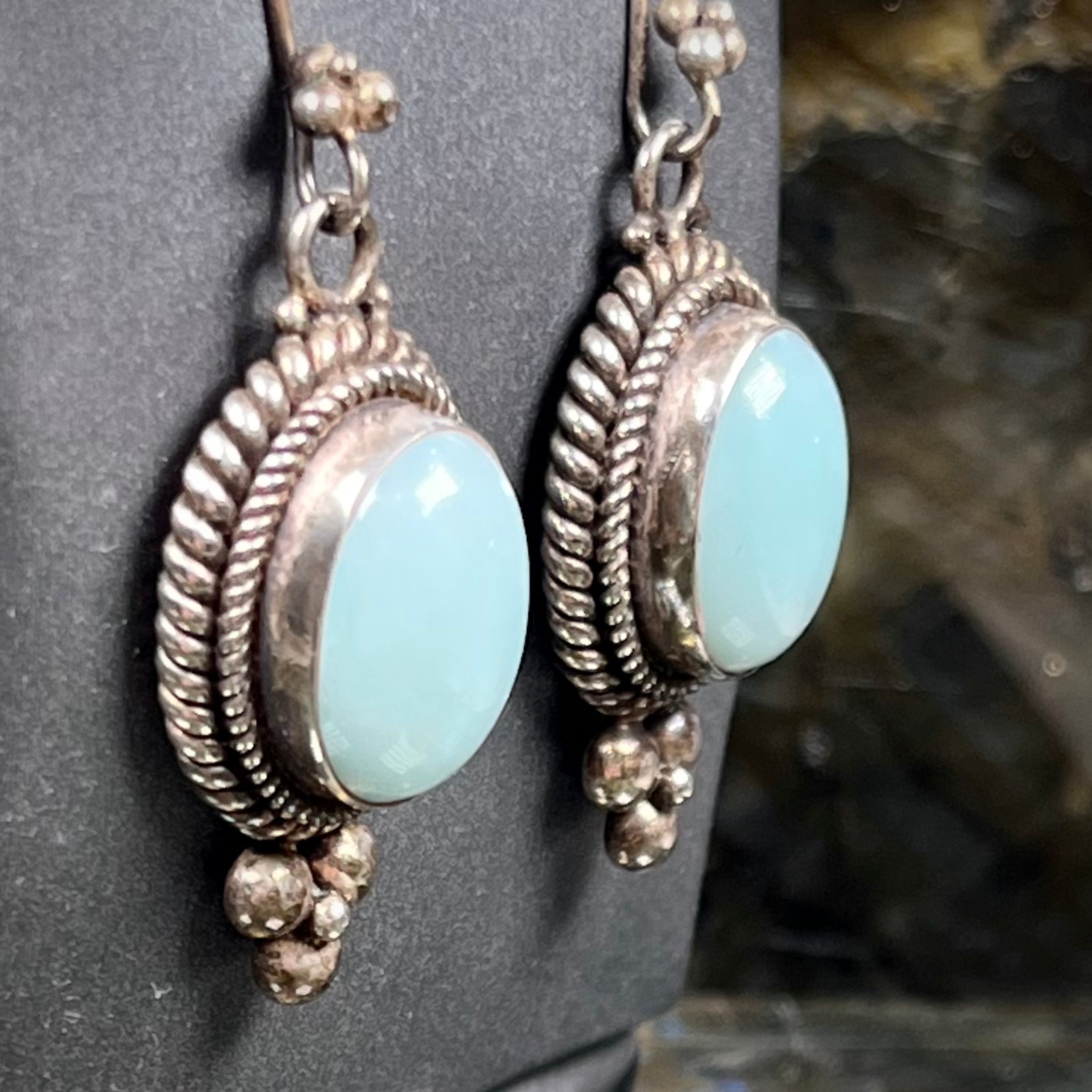 A pair of silver wire dangle earrings set with blue agate stones.  The earrings have a braided rope design.