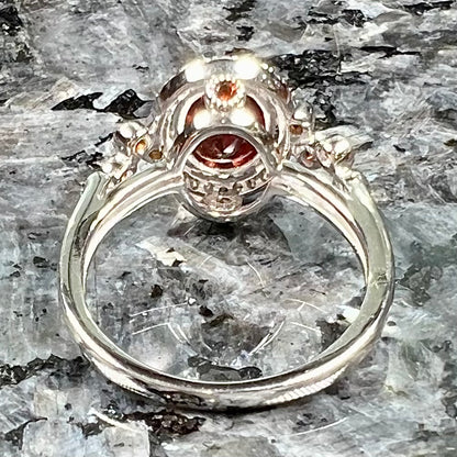 A silver garnet and CZ halo ring.  The center stone is a red almandine garnet, and the side garnets are orange.