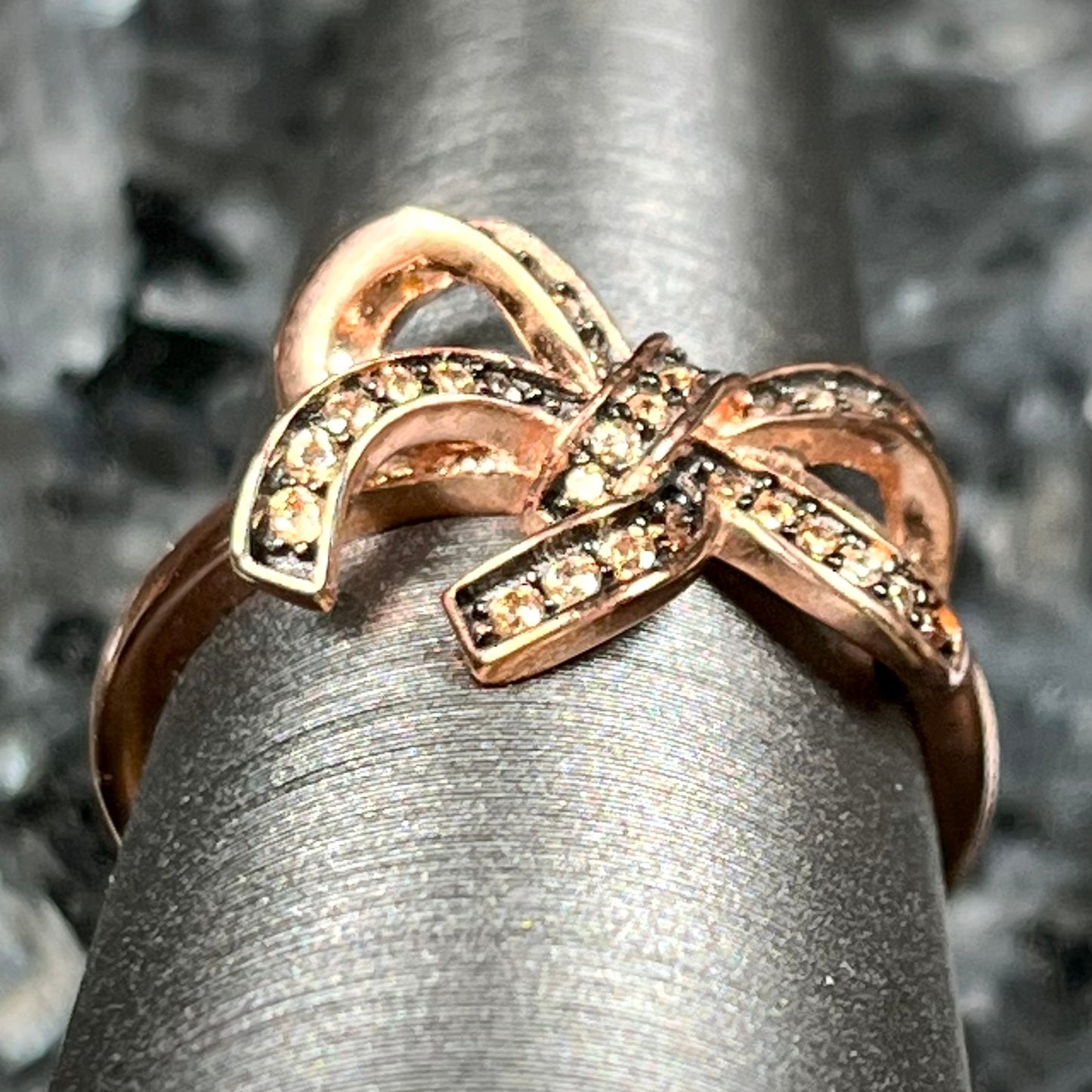 A rose gold colored bow ring.  The bow is tied in a knot, and the knot is set with cognac cubic zirconia.