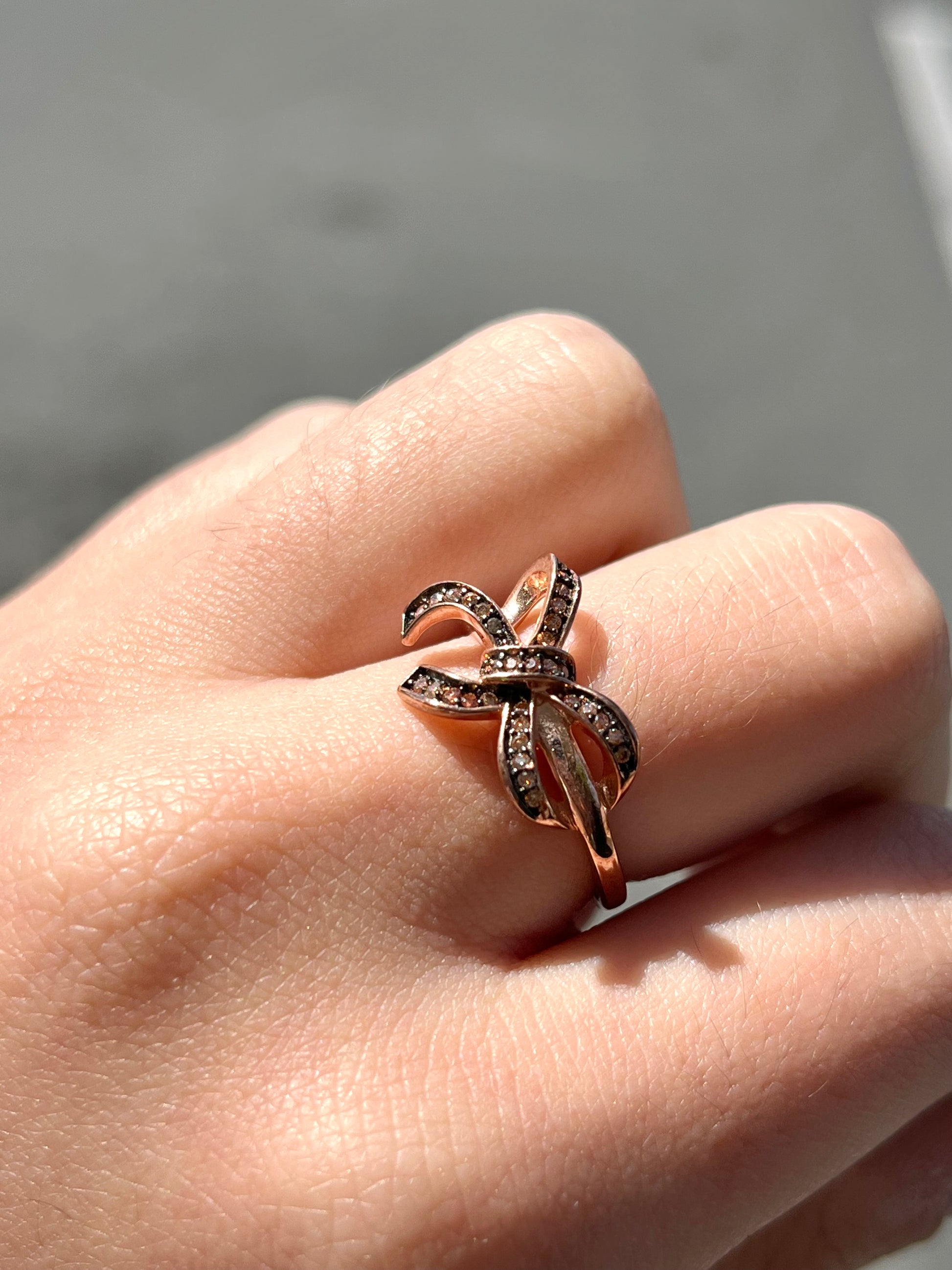 A rose gold colored bow ring.  The bow is tied in a knot, and the knot is set with cognac cubic zirconia.