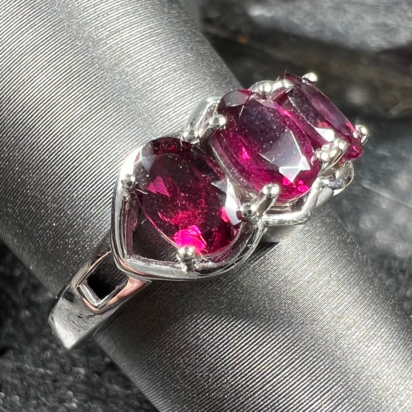 A three stone past, present, and future purple faceted oval cut rhodolite garnet ring.