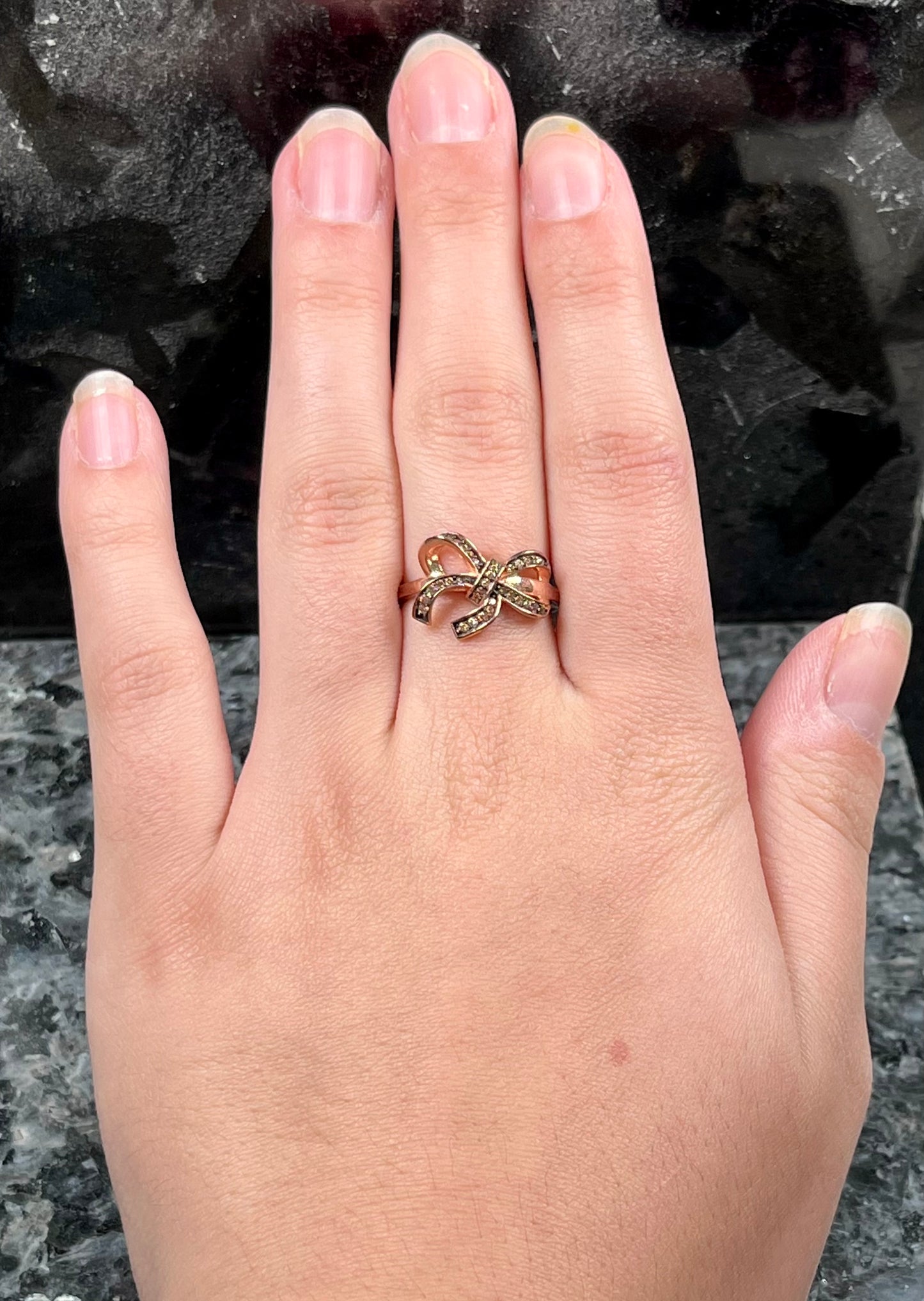 A rose gold colored bow ring.  The bow is tied in a knot, and the knot is set with cognac cubic zirconia.