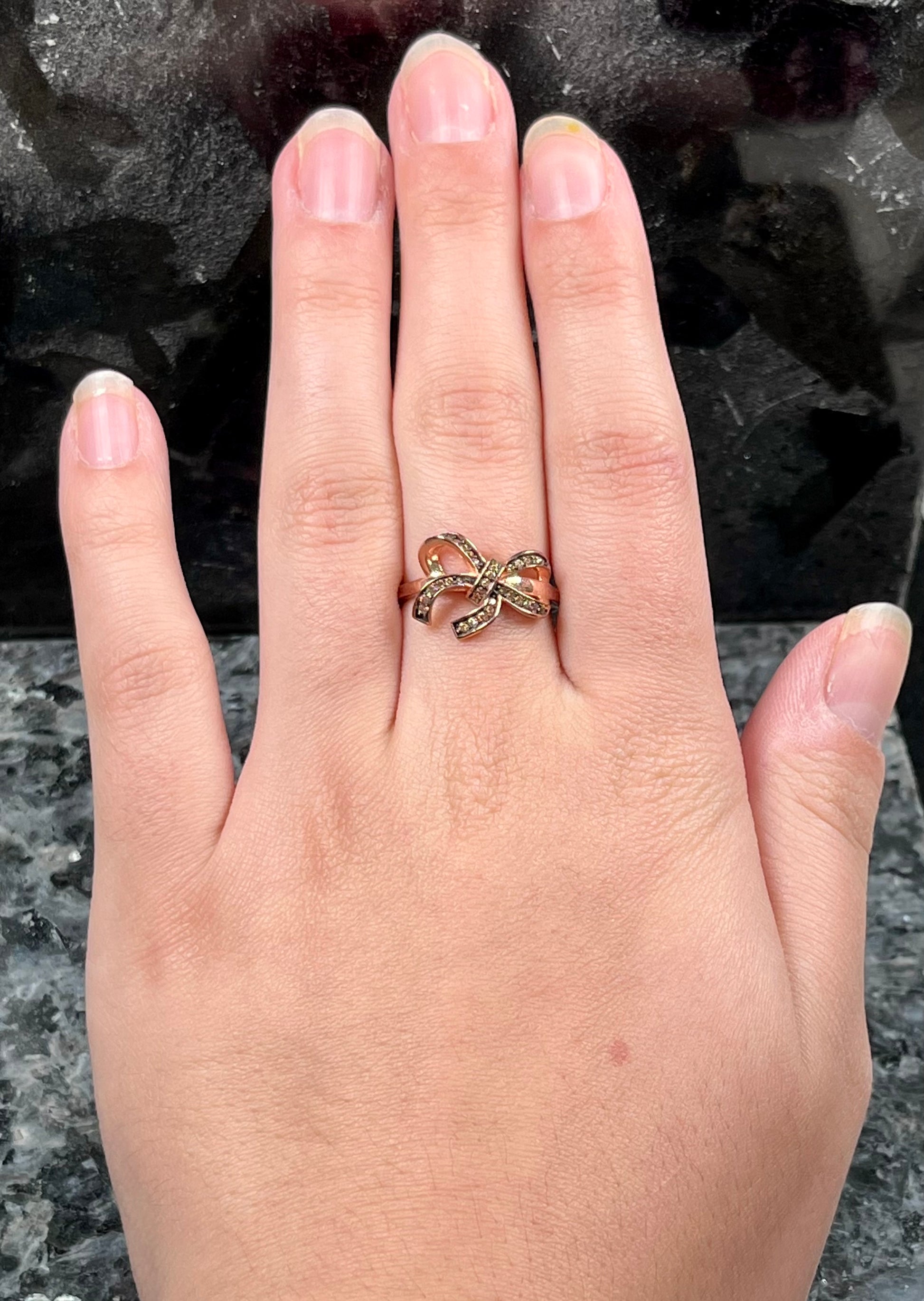 A rose gold colored bow ring.  The bow is tied in a knot, and the knot is set with cognac cubic zirconia.