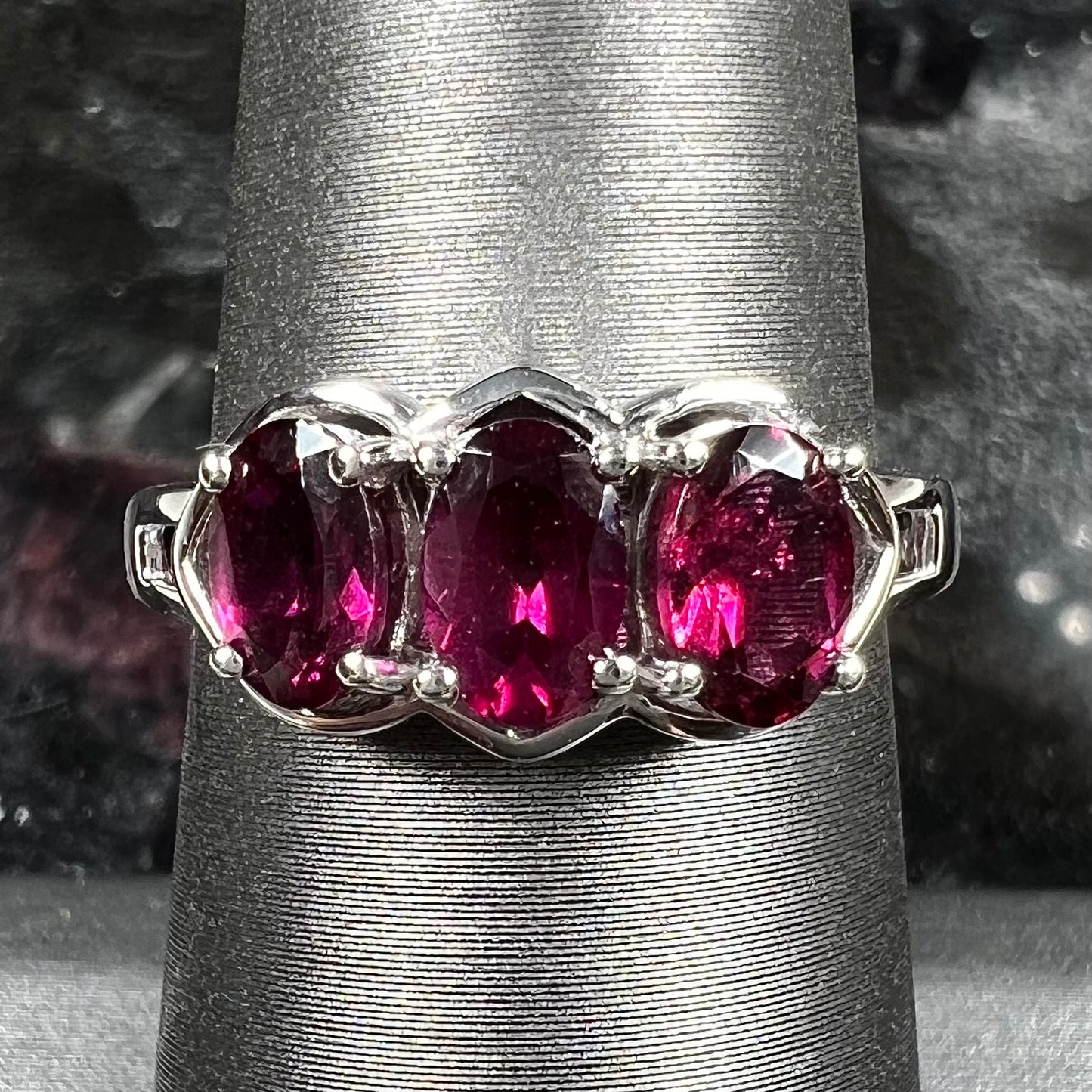 A three stone past, present, and future purple faceted oval cut rhodolite garnet ring.