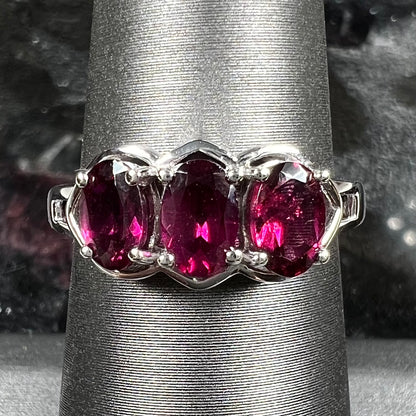 A three stone past, present, and future purple faceted oval cut rhodolite garnet ring.