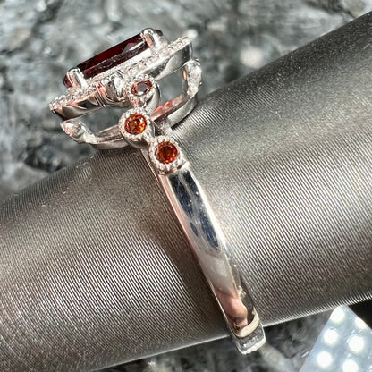 A silver garnet and CZ halo ring.  The center stone is a red almandine garnet, and the side garnets are orange.