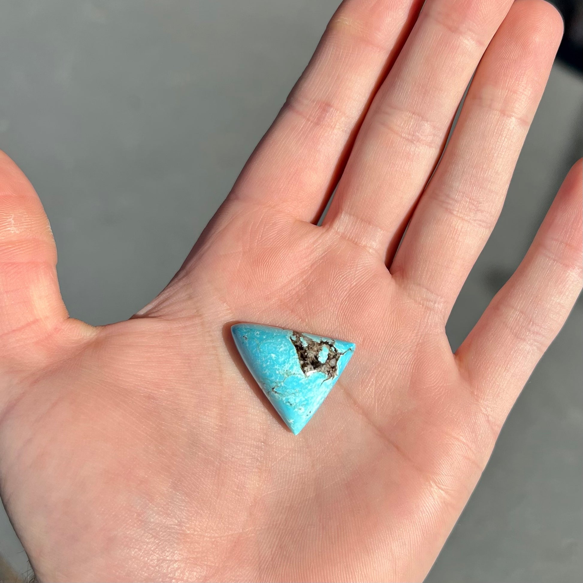 A triangular cabochon cut turquoise stone from the Valley Blue mine in Lander County, Nevada.  The stone has a black matrix.