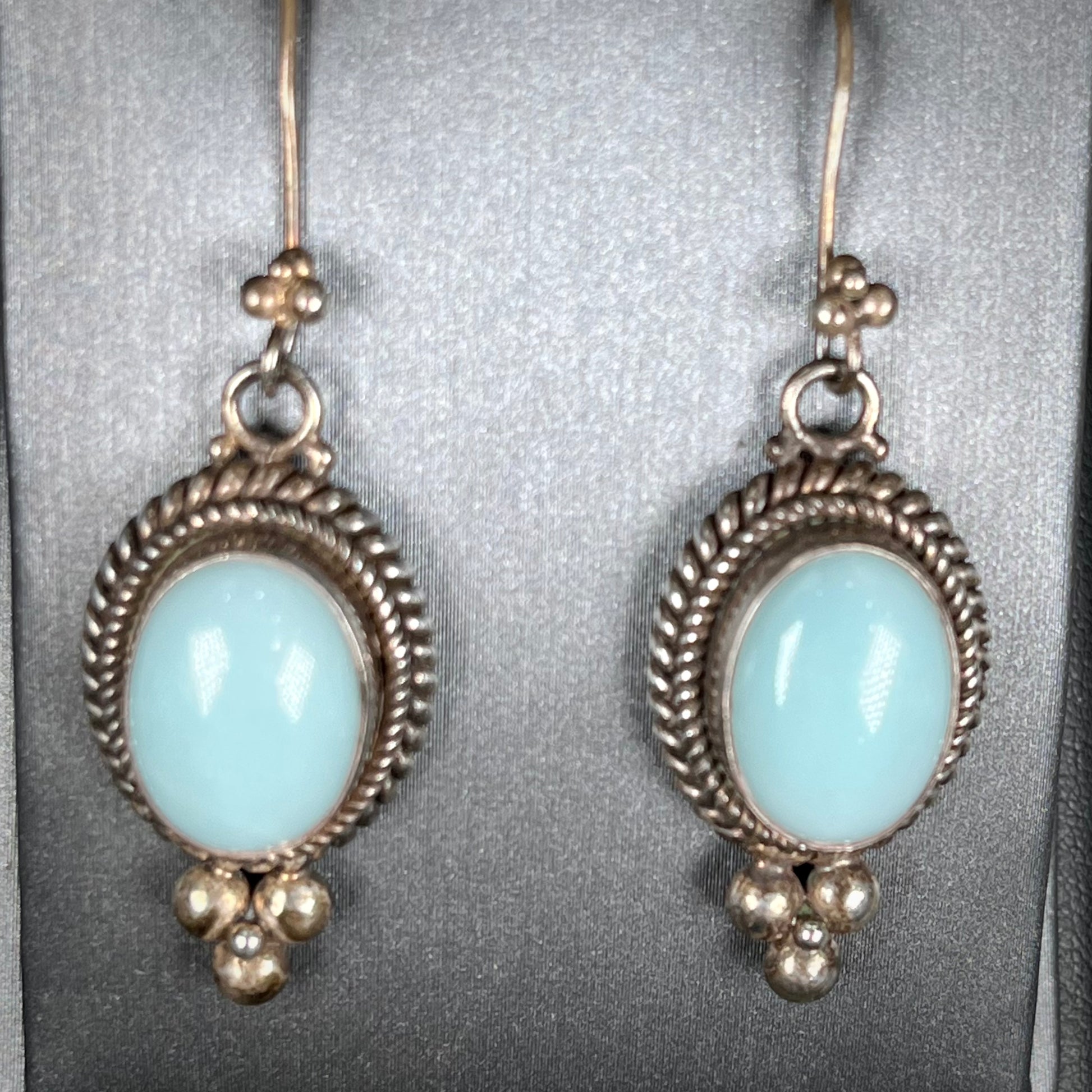A pair of silver wire dangle earrings set with blue agate stones.  The earrings have a braided rope design.