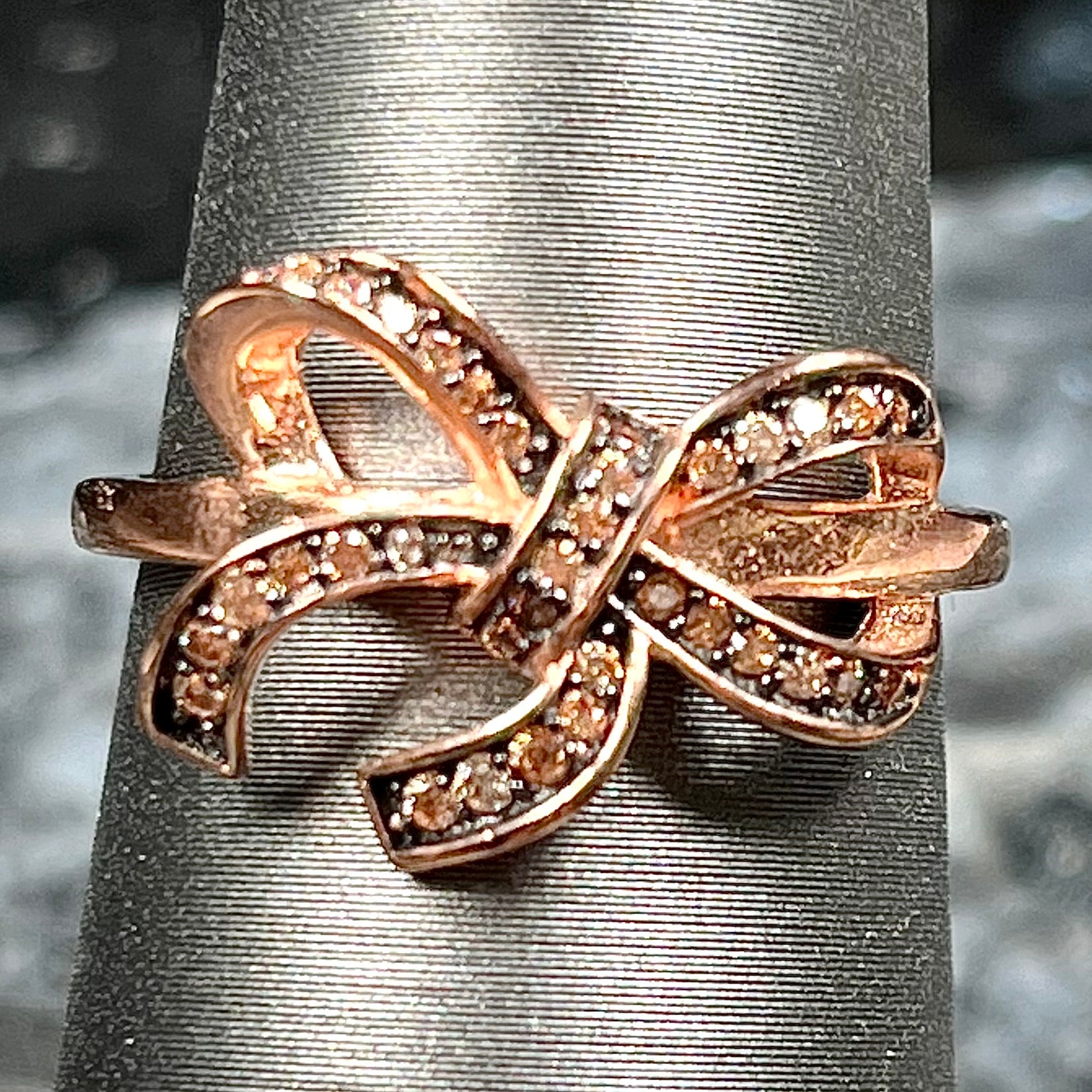 A rose gold colored bow ring.  The bow is tied in a knot, and the knot is set with cognac cubic zirconia.