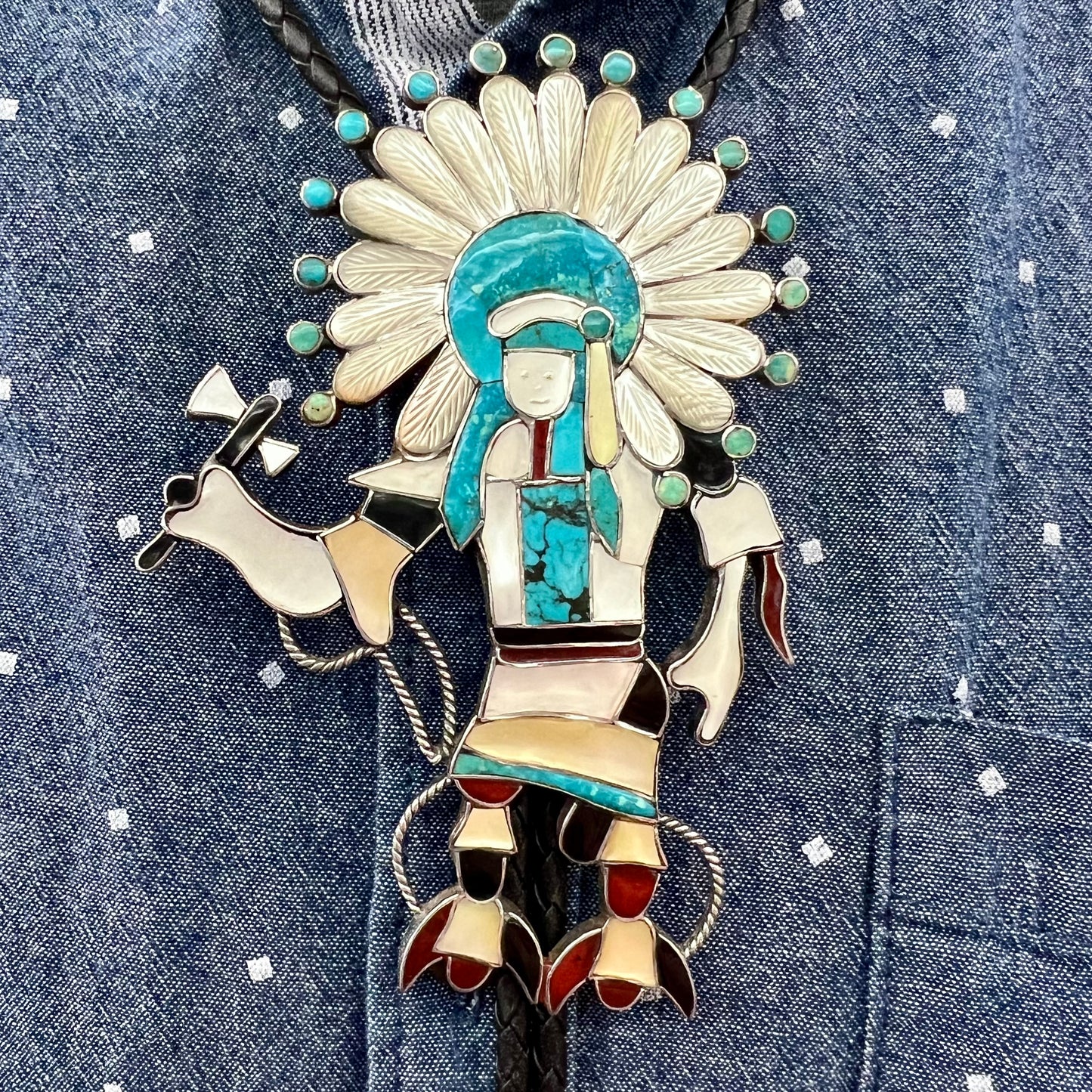 A Zuni Indian-made bolo tie featuring the motif of a kachina, inlaid with natural turquoise, mother of pearl, jet, and jasper stones.