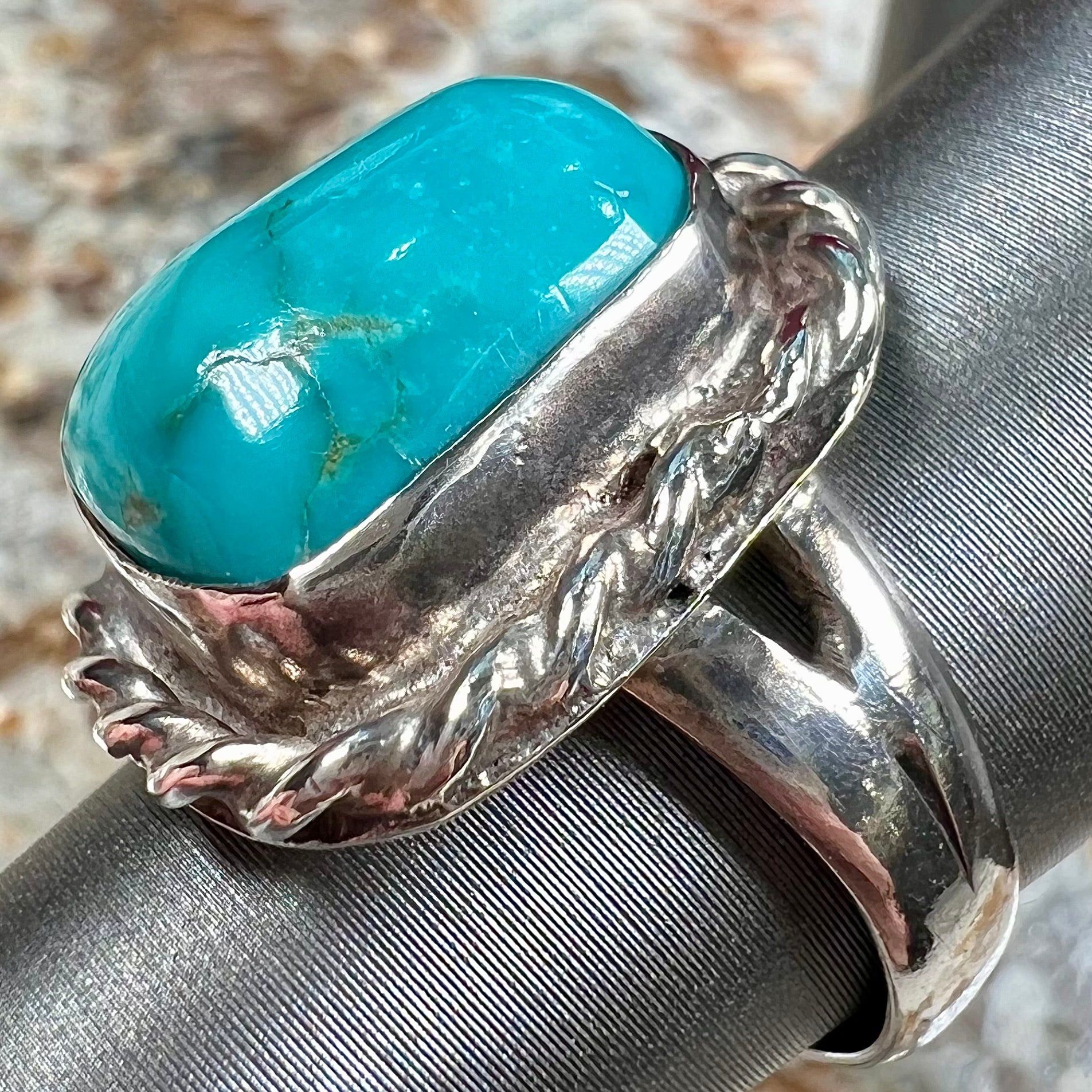 A sterling silver turquoise split shank ring.  There is a handmade silver rope around the turquoise.