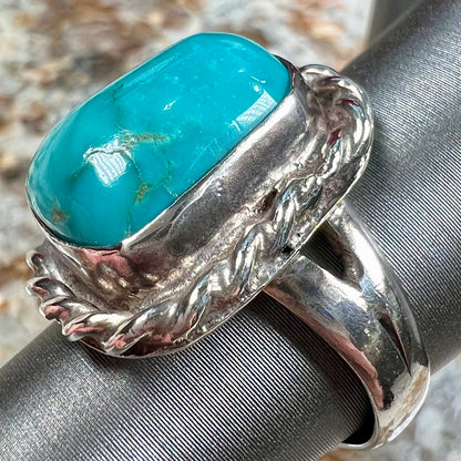 A sterling silver turquoise split shank ring.  There is a handmade silver rope around the turquoise.