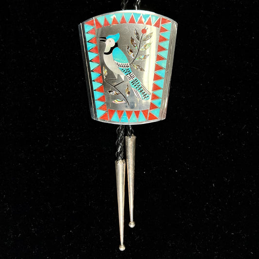 A turquoise and coral inlay bolo tie featuring the motif of a blue jay bird, handmade by Zuni artists Dennis and Nancy Edaakie.