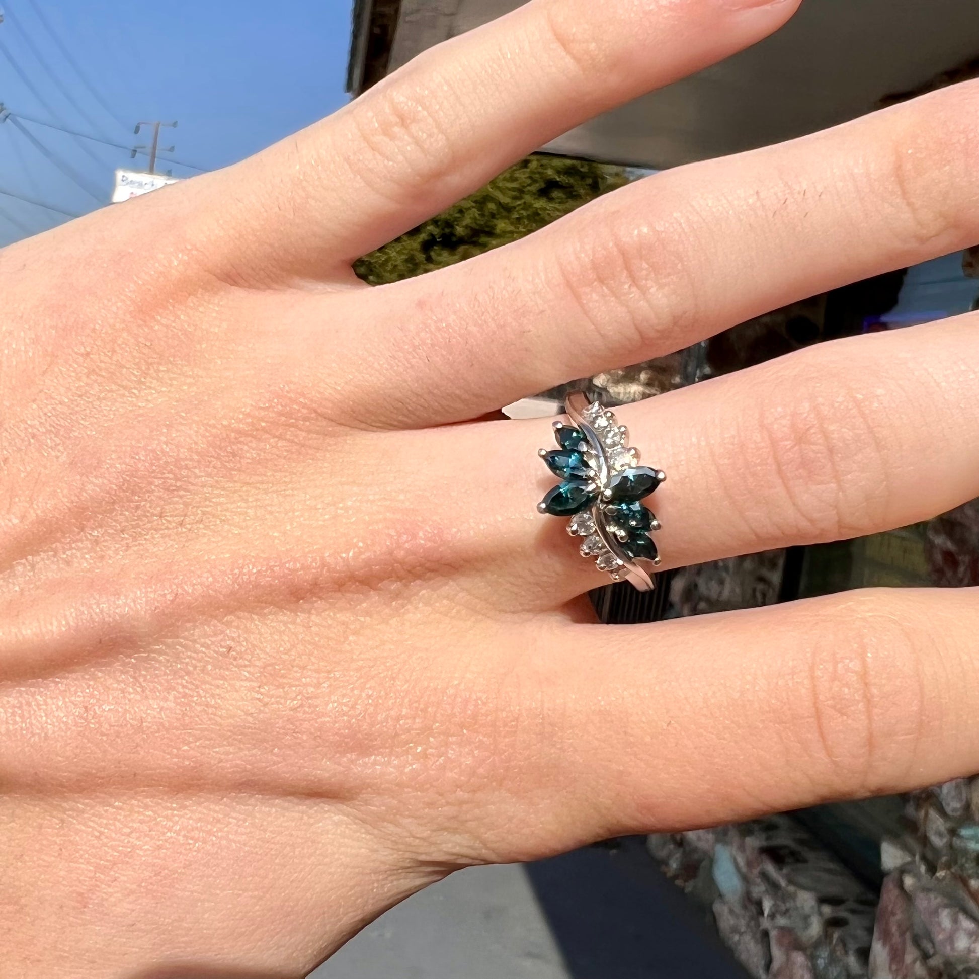 A white gold diamond cluster ring set with blue marquise cut and white round cut diamonds.