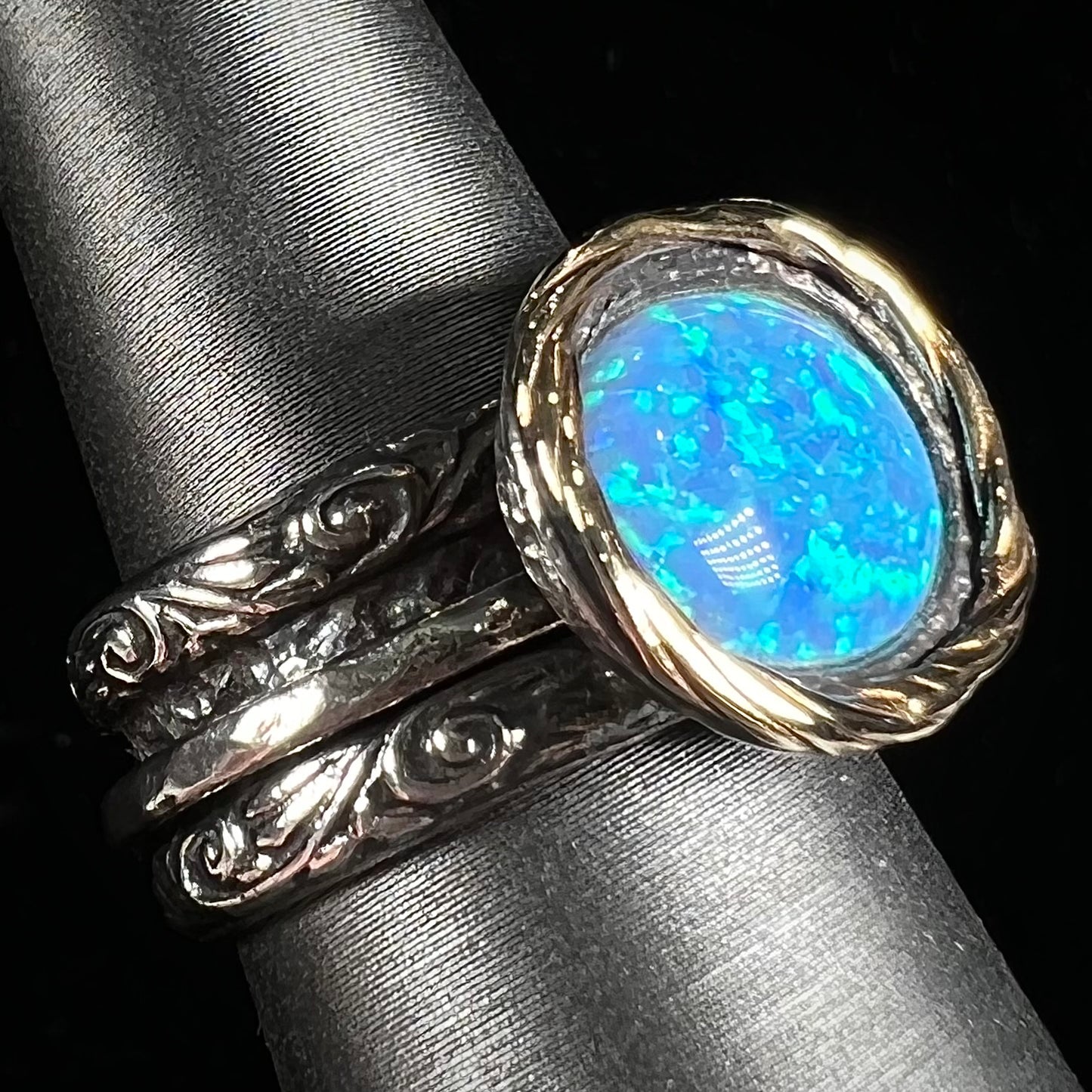 A filigree etched two tone silver and gold spinner ring set with a lab created black opal.