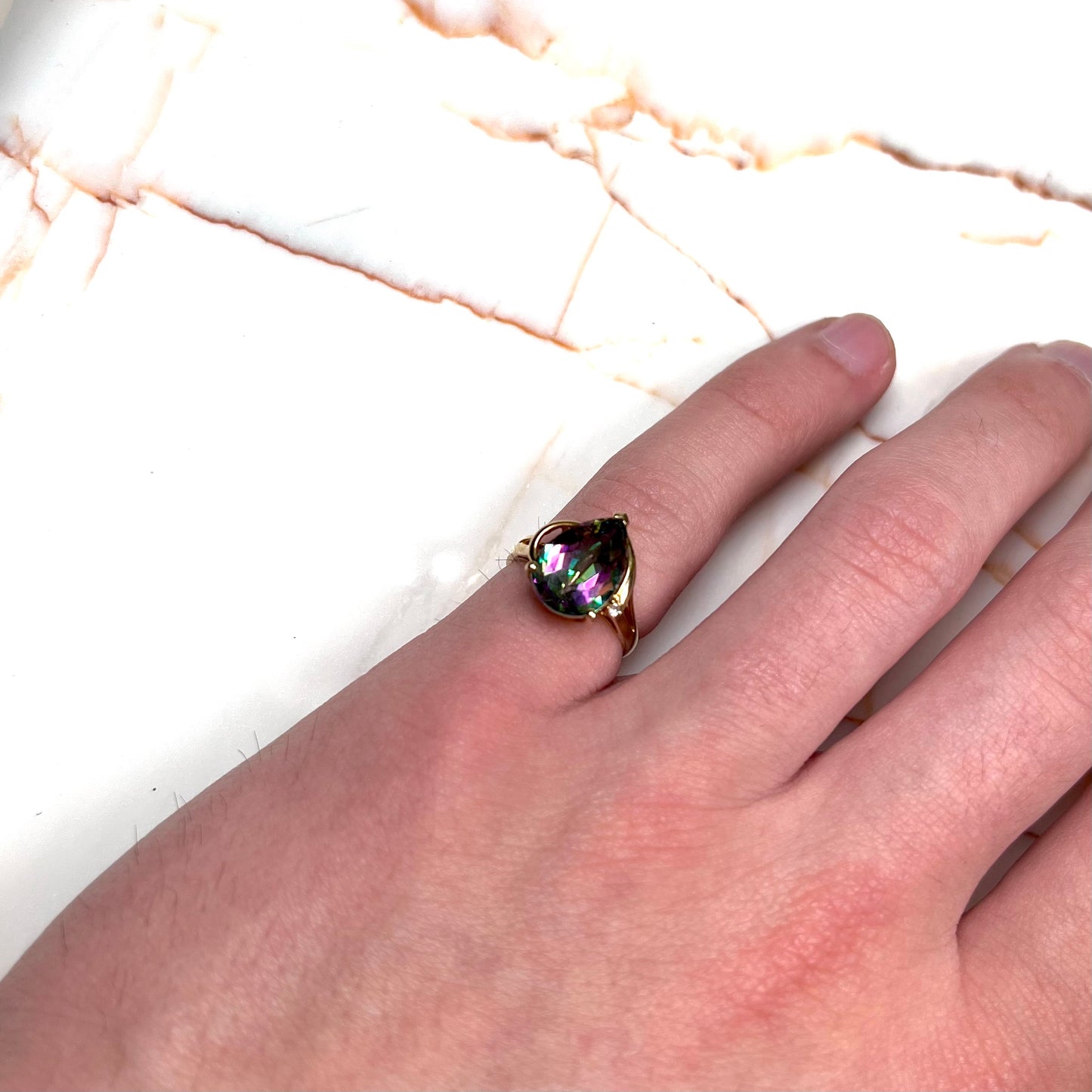 Pear shape green and pink mystic topaz set in a yellow gold ring with a single round diamond.