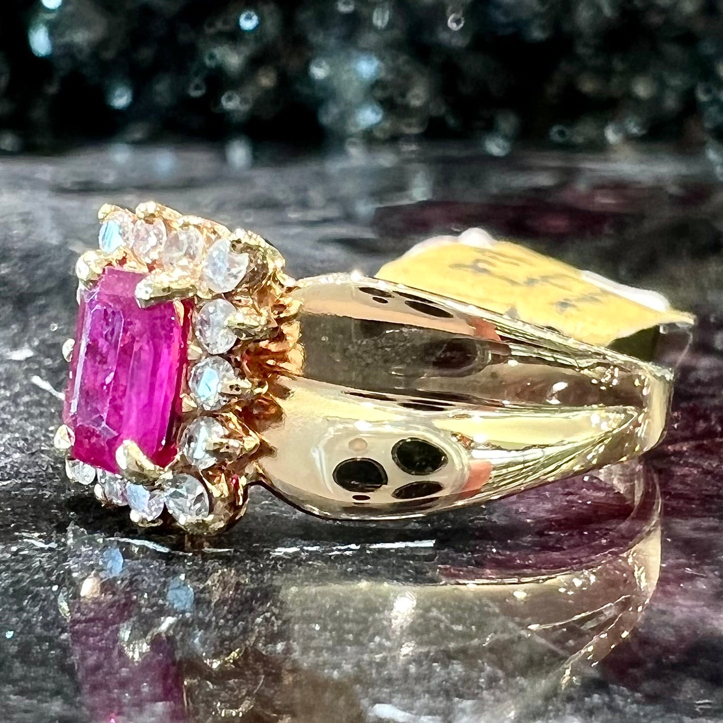 A yellow gold ring set with an emerald cut red ruby surrounded by a halo of round diamonds.