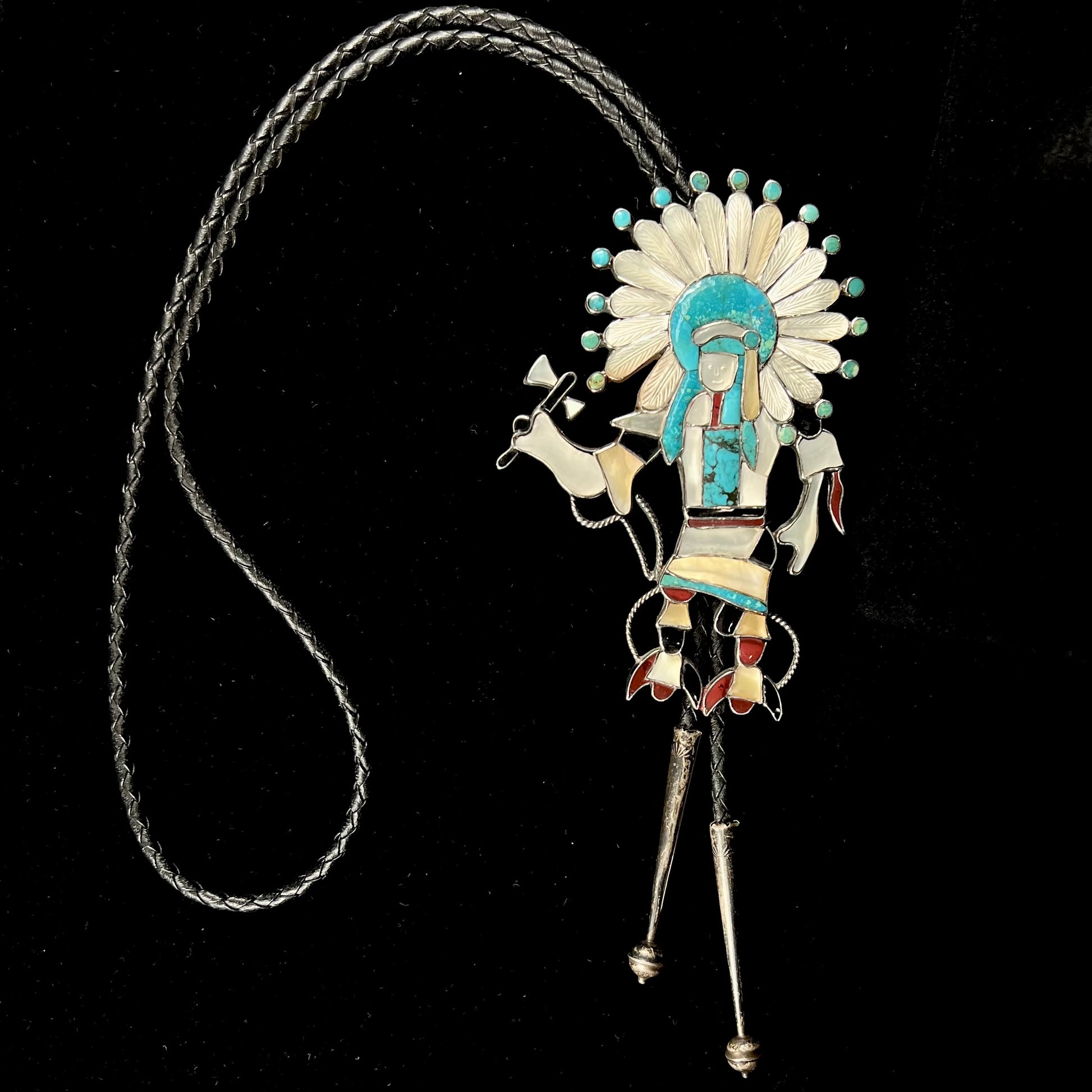 A Zuni Indian-made bolo tie featuring the motif of a kachina, inlaid with natural turquoise, mother of pearl, jet, and jasper stones.