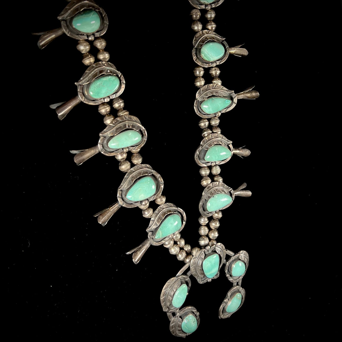 A handmade silver Navajo style squash blossom necklace set with green Kingman turquoise.