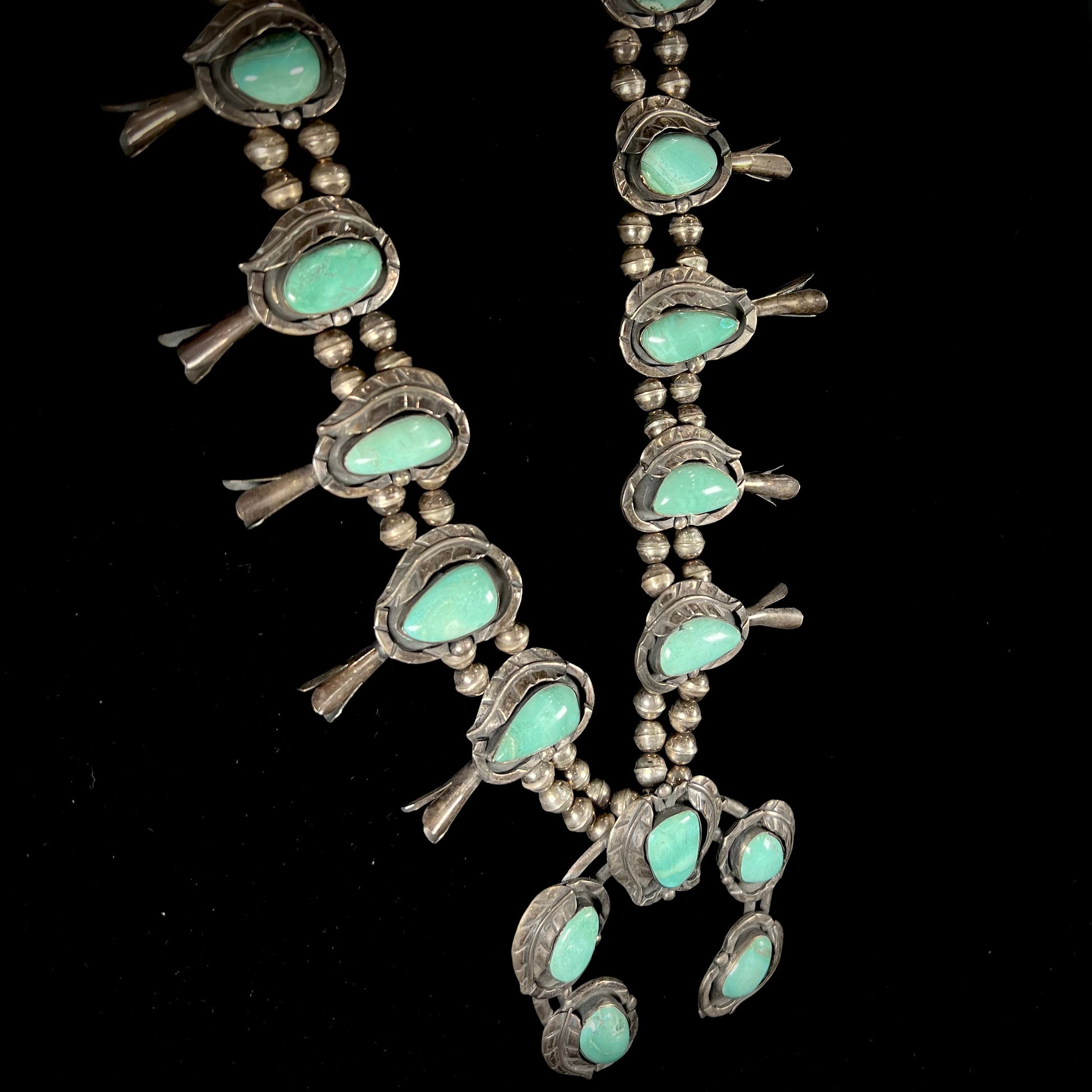 A handmade silver Navajo style squash blossom necklace set with green Kingman turquoise.