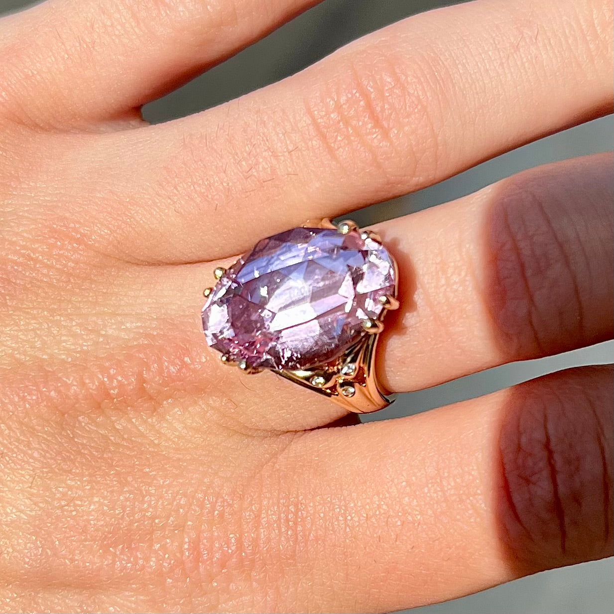 A large, pink kunzite is prong set into a 14kt yellow gold basket-style ring mounting with three diamonds flush set into the design on each side.