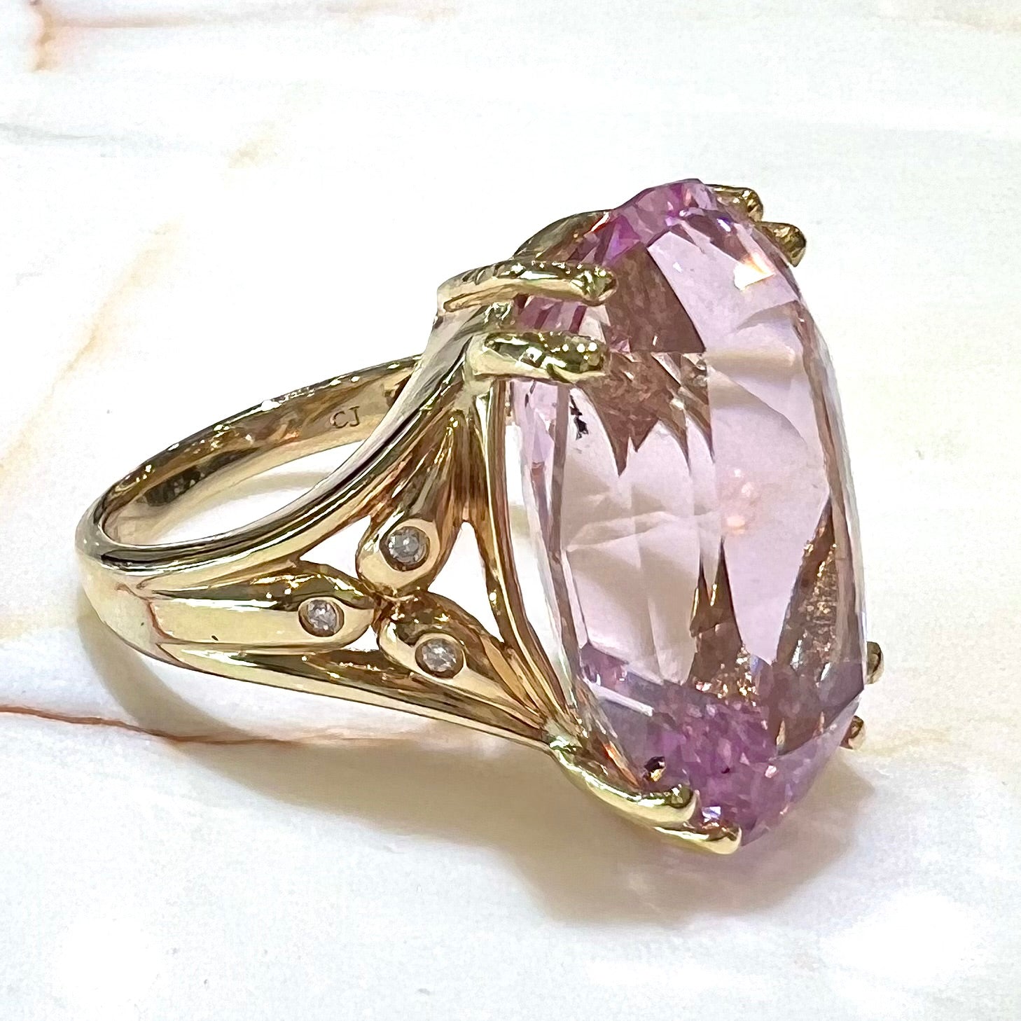 A large, pink kunzite is prong set into a 14kt yellow gold basket-style ring mounting with three diamonds flush set into the design on each side.