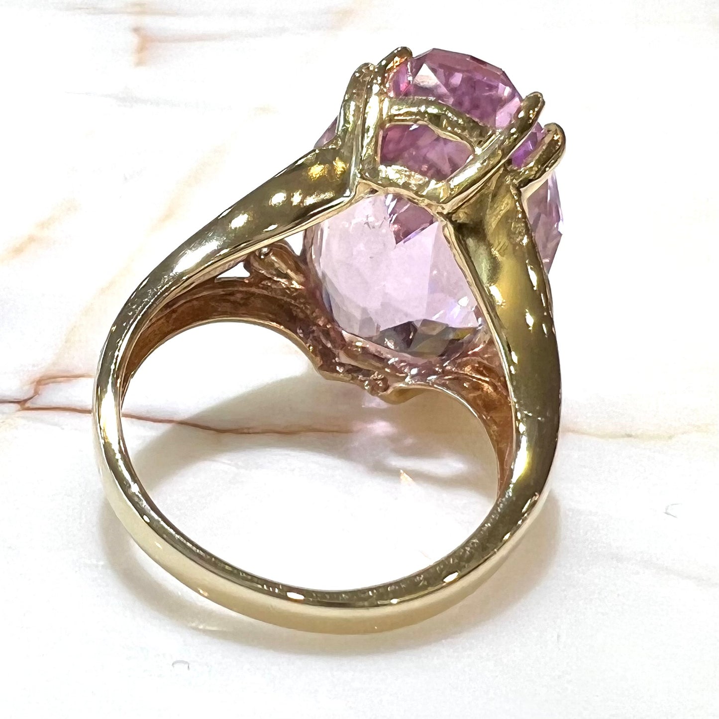 A large, pink kunzite is prong set into a 14kt yellow gold basket-style ring mounting with three diamonds flush set into the design on each side.