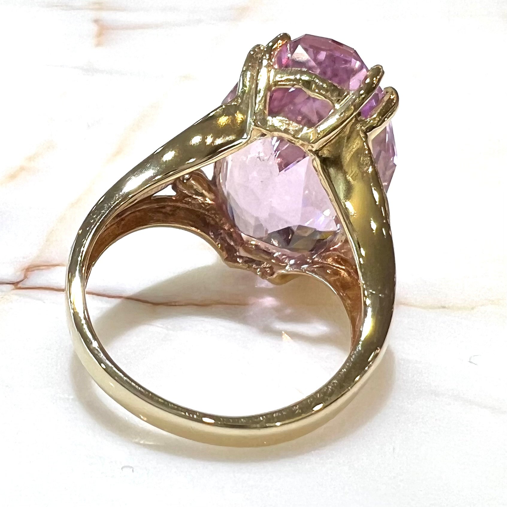 A large, pink kunzite is prong set into a 14kt yellow gold basket-style ring mounting with three diamonds flush set into the design on each side.