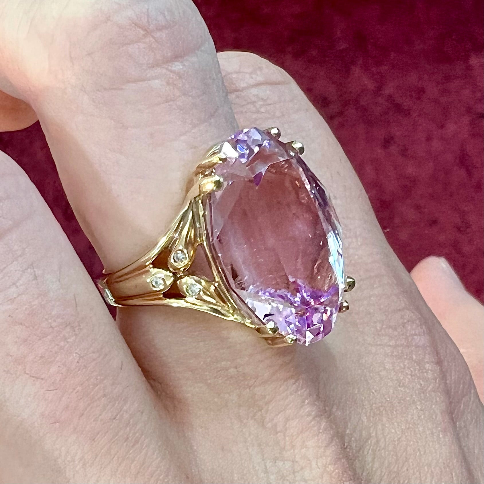 A large, pink kunzite is prong set into a 14kt yellow gold basket-style ring mounting with three diamonds flush set into the design on each side.