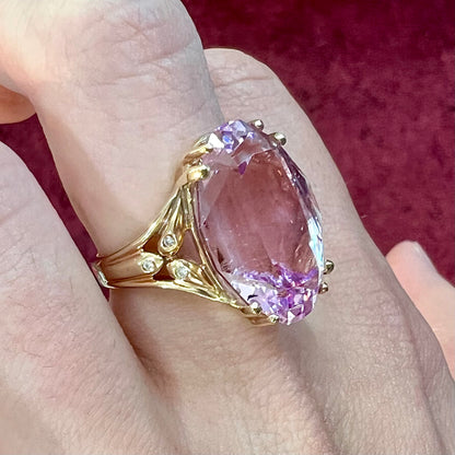 A large, pink kunzite is prong set into a 14kt yellow gold basket-style ring mounting with three diamonds flush set into the design on each side.