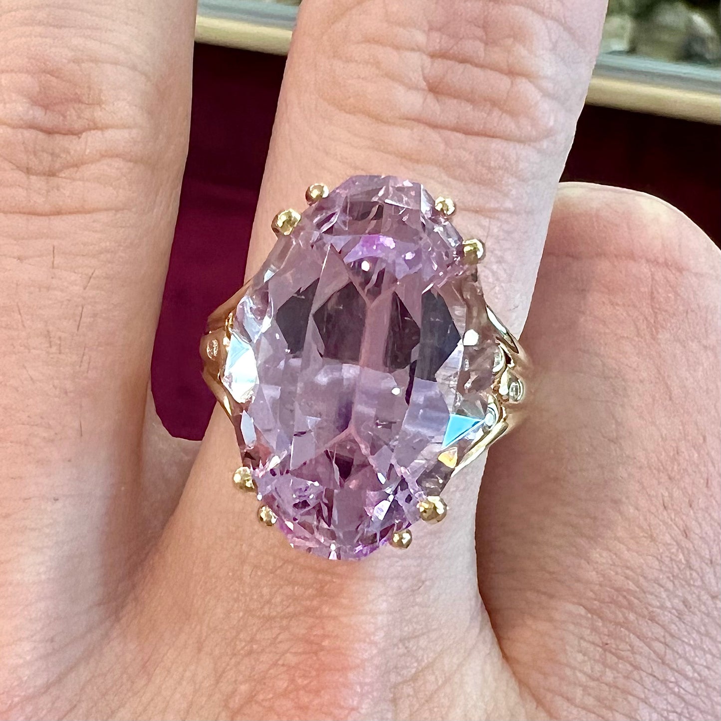 A large, pink kunzite is prong set into a 14kt yellow gold basket-style ring mounting with three diamonds flush set into the design on each side.