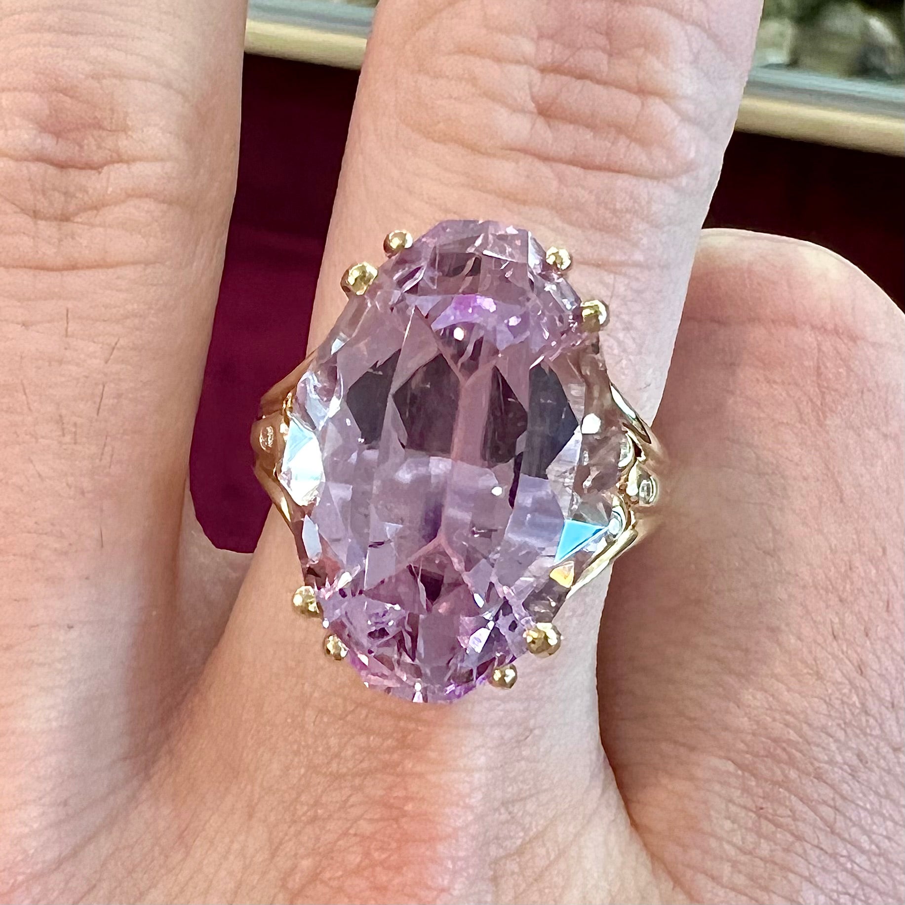 A large, pink kunzite is prong set into a 14kt yellow gold basket-style ring mounting with three diamonds flush set into the design on each side.