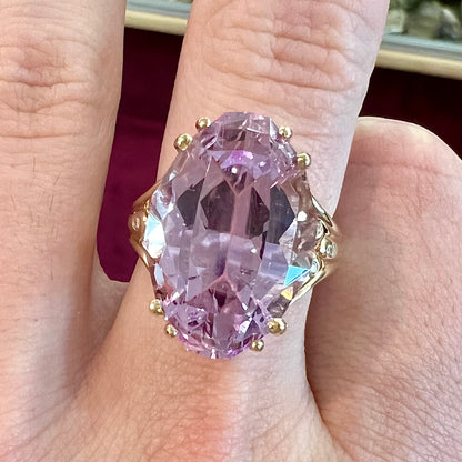 A large, pink kunzite is prong set into a 14kt yellow gold basket-style ring mounting with three diamonds flush set into the design on each side.