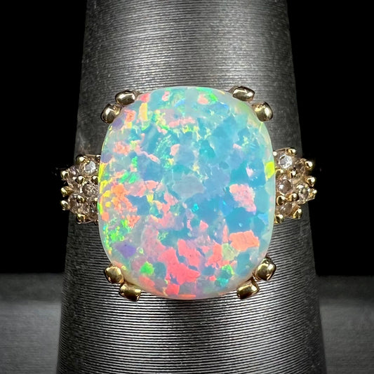 A ladies' yellow gold laboratory created, synthetic, cushion cut opal ring set with natural diamond accents.