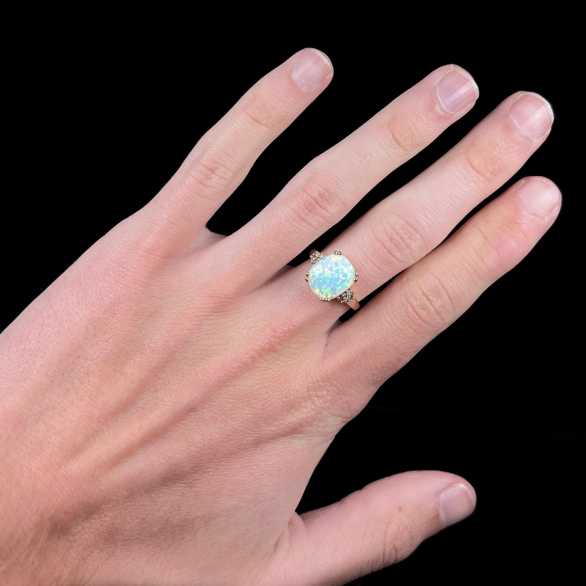 A ladies' yellow gold laboratory created, synthetic, cushion cut opal ring set with natural diamond accents.