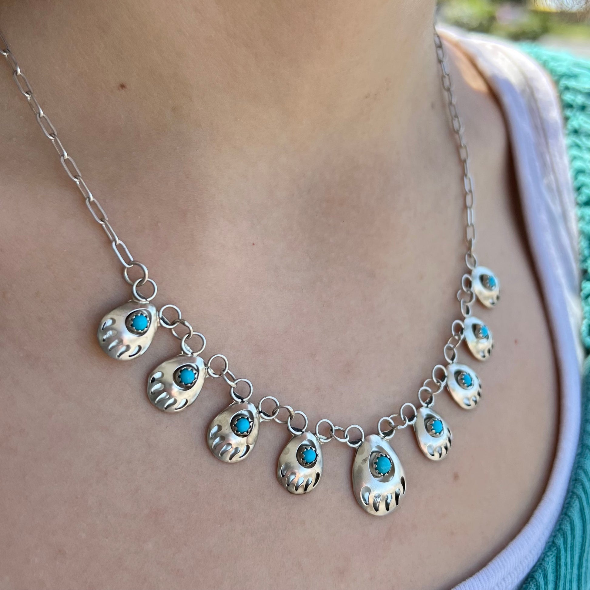 A silver turquoise necklace handmade with nine silver bear paws set with round turquoise stones.
