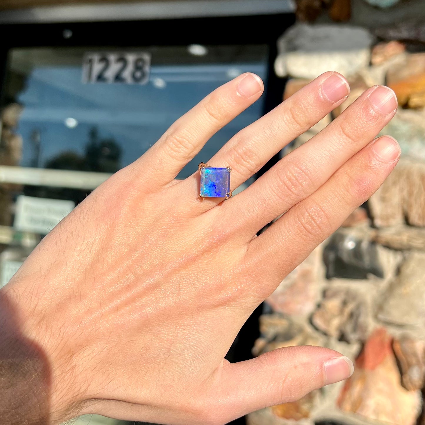 A ladies' boulder opal solitaire ring, handmade in yellow gold.  The stone is purple with flashes of blue, aqua, and green.