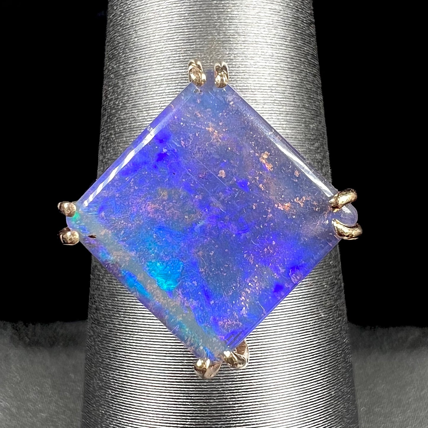 A ladies' boulder opal solitaire ring, handmade in yellow gold.  The stone is purple with flashes of blue, aqua, and green.