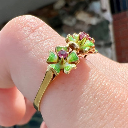A gold ladies' ring in the motif of three flowers set with round ruby centers and green enameled petals.