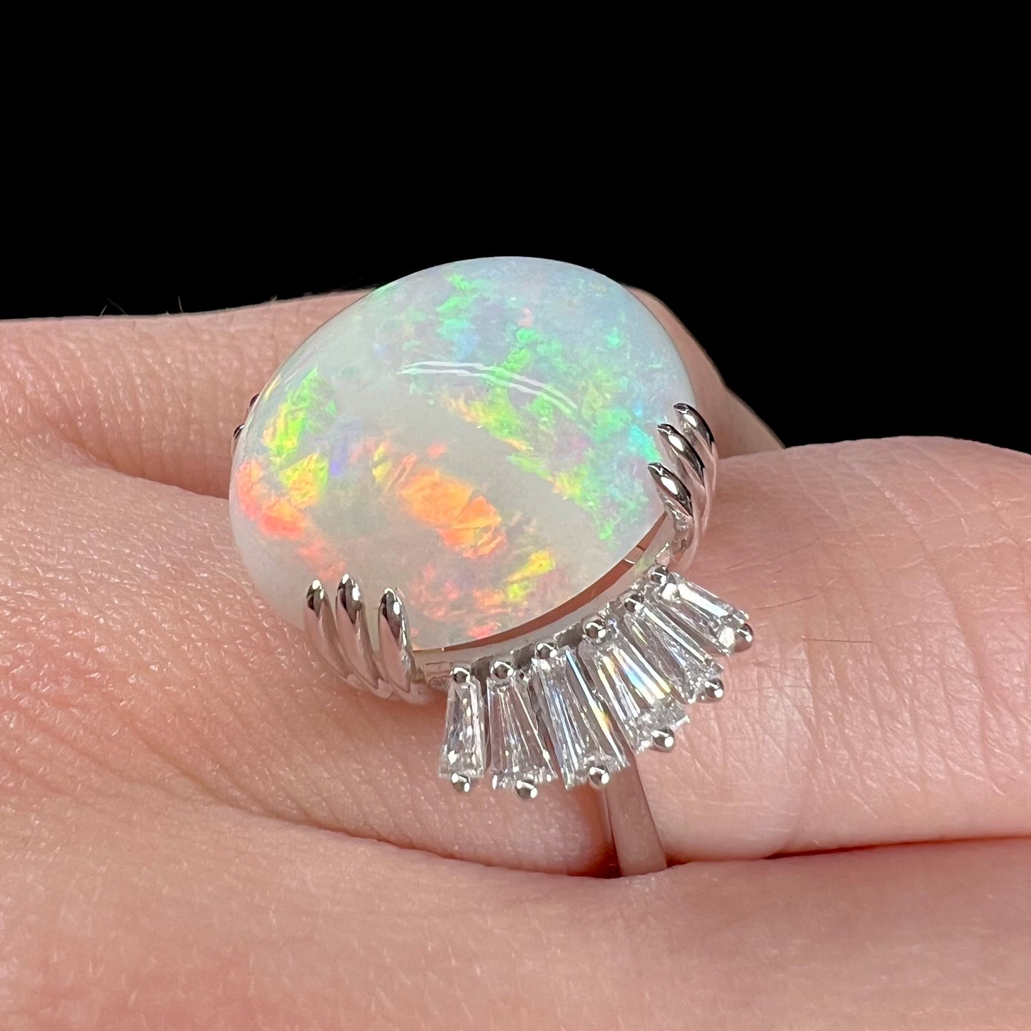 An oval cabochon cut opal mounted in a ladies' white gold ring between tapered baguette cut diamonds.