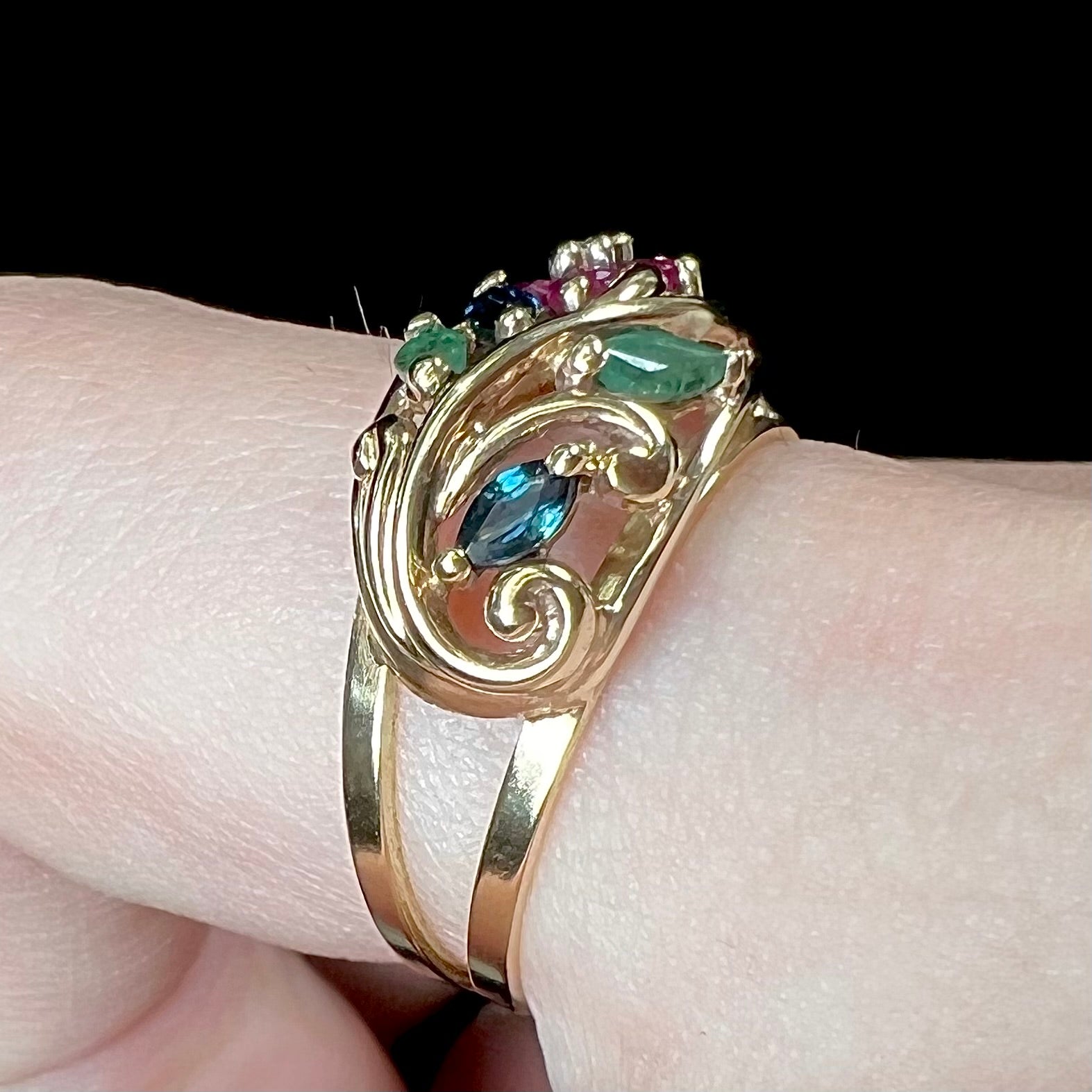 A yellow gold ladies' ring featuring the motif of a flower with leaves set with emeralds, rubies, sapphires, and a  diamond.