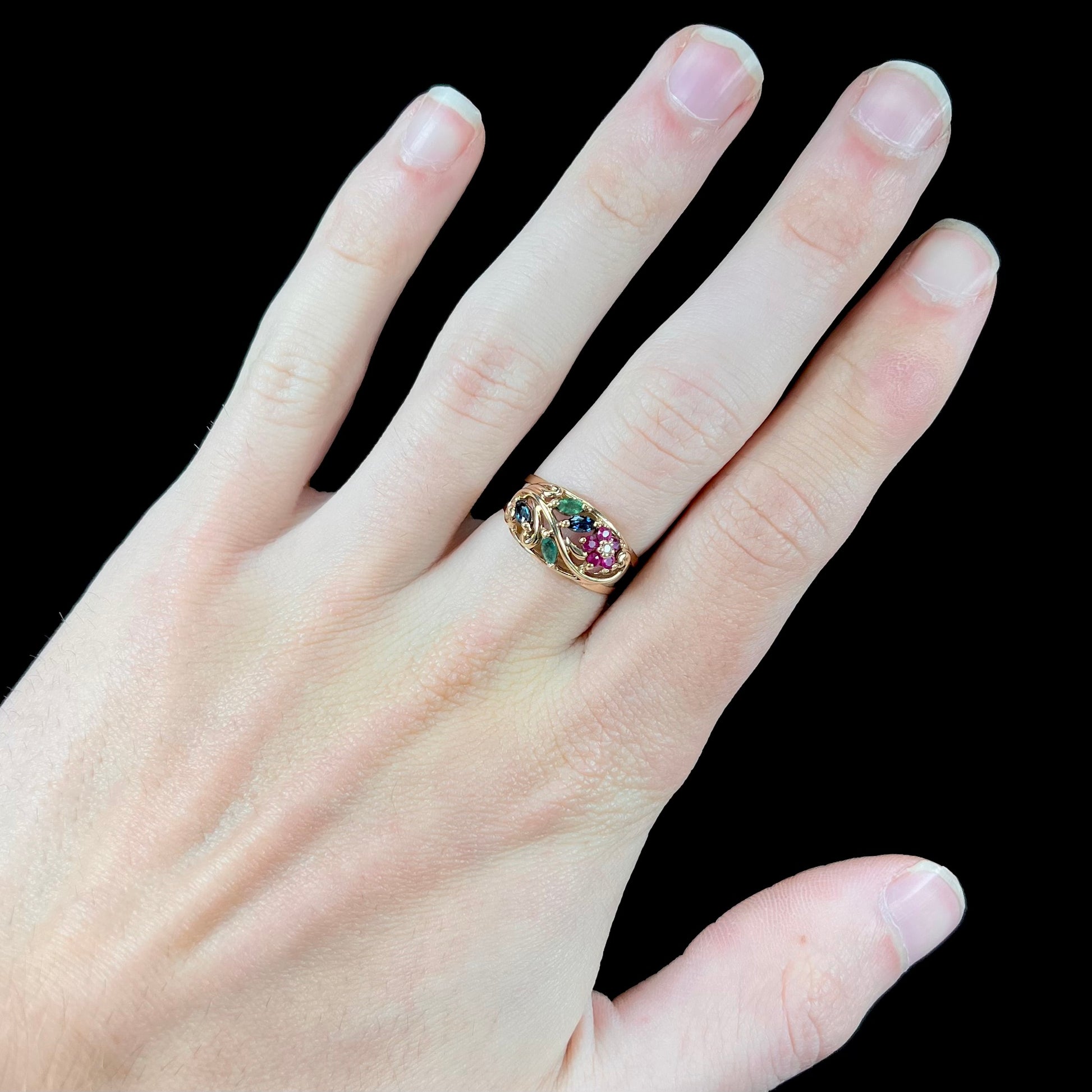 A yellow gold ladies' ring featuring the motif of a flower with leaves set with emeralds, rubies, sapphires, and a  diamond.