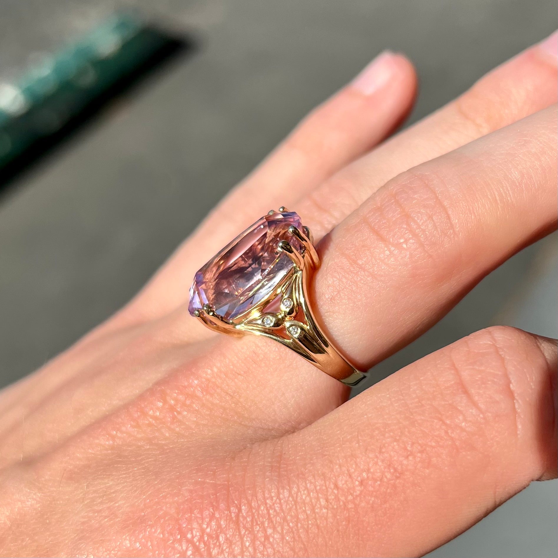 A large, pink kunzite is prong set into a 14kt yellow gold basket-style ring mounting with three diamonds flush set into the design on each side.
