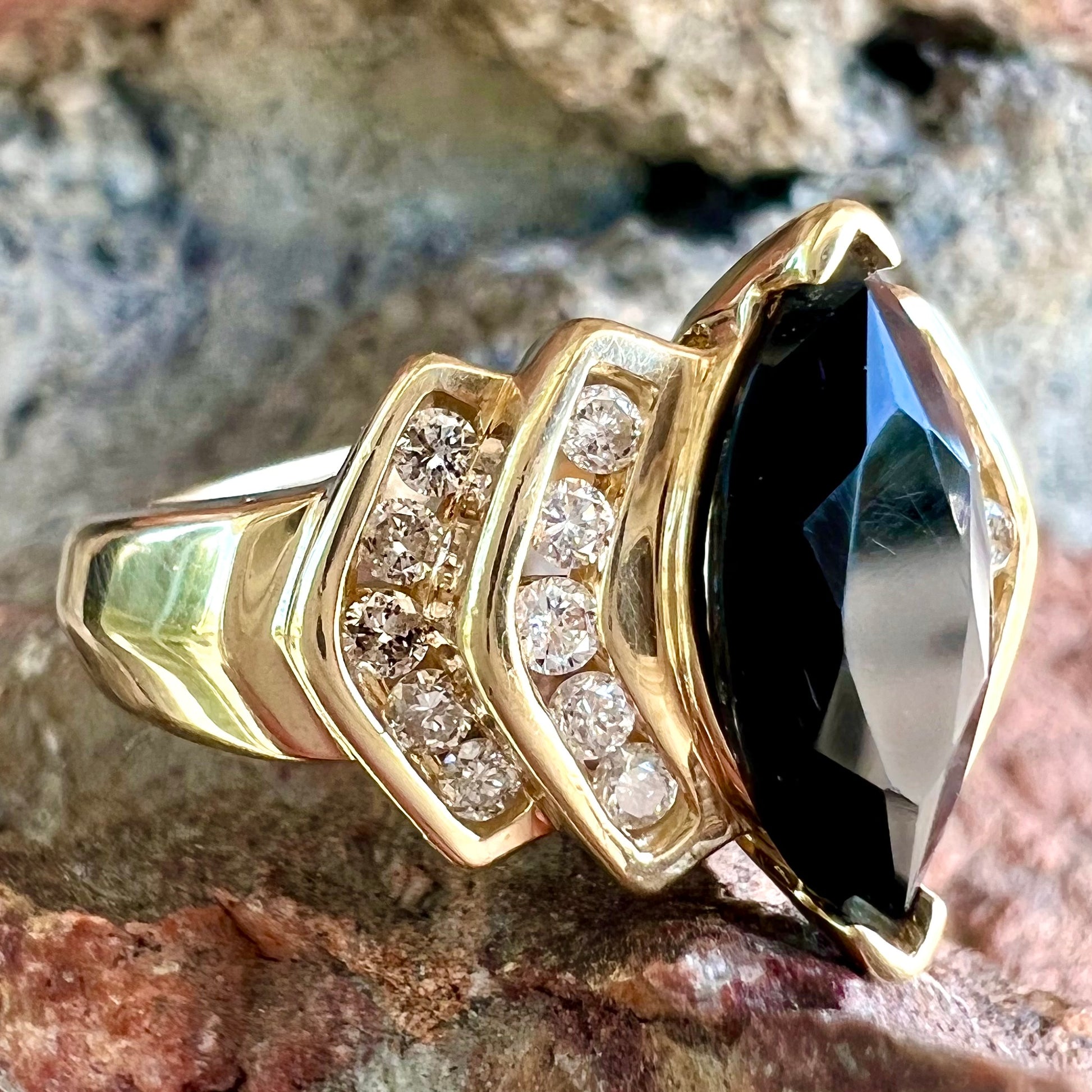A gold, marquise cut black sapphire ring set with channel set diamond accents.