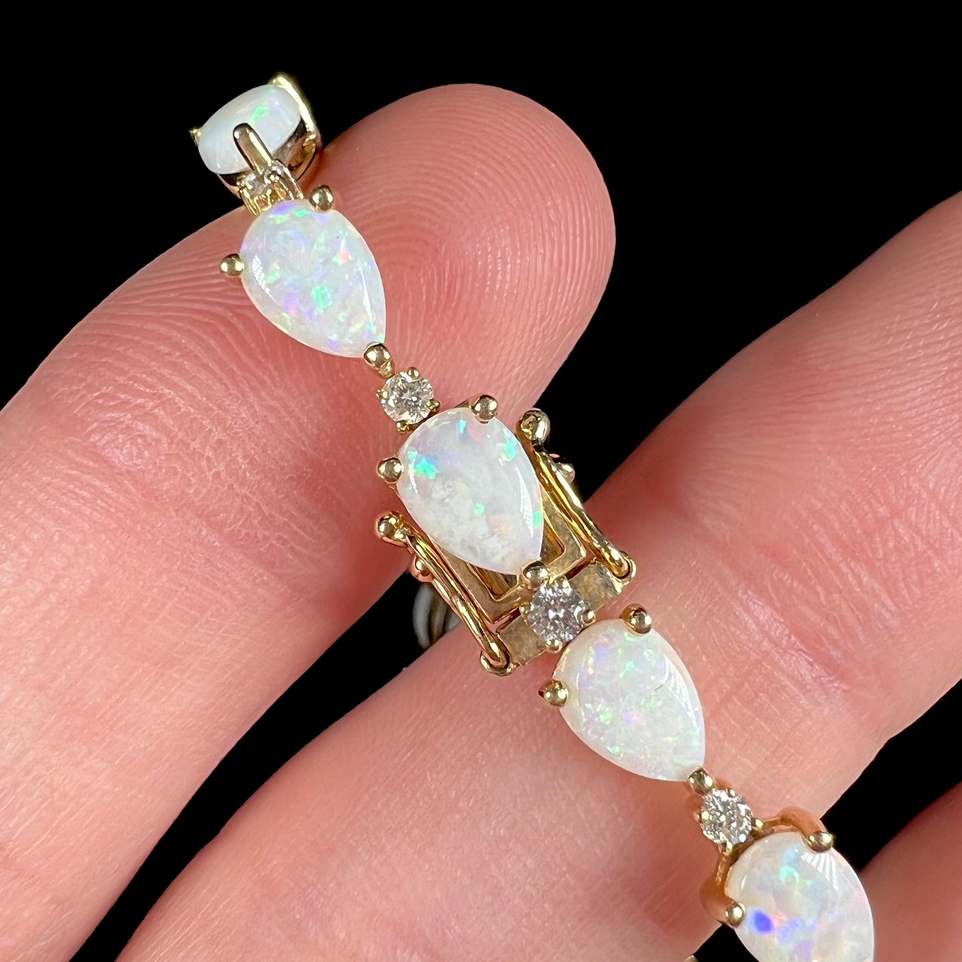 A ladies' gold tennis style bracelet set with pear shaped white crystal opals and diamonds.