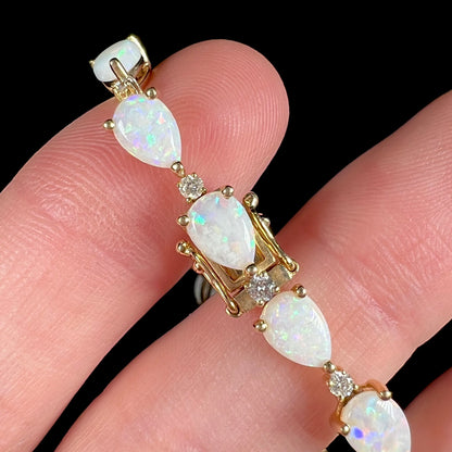 A ladies' gold tennis style bracelet set with pear shaped white crystal opals and diamonds.
