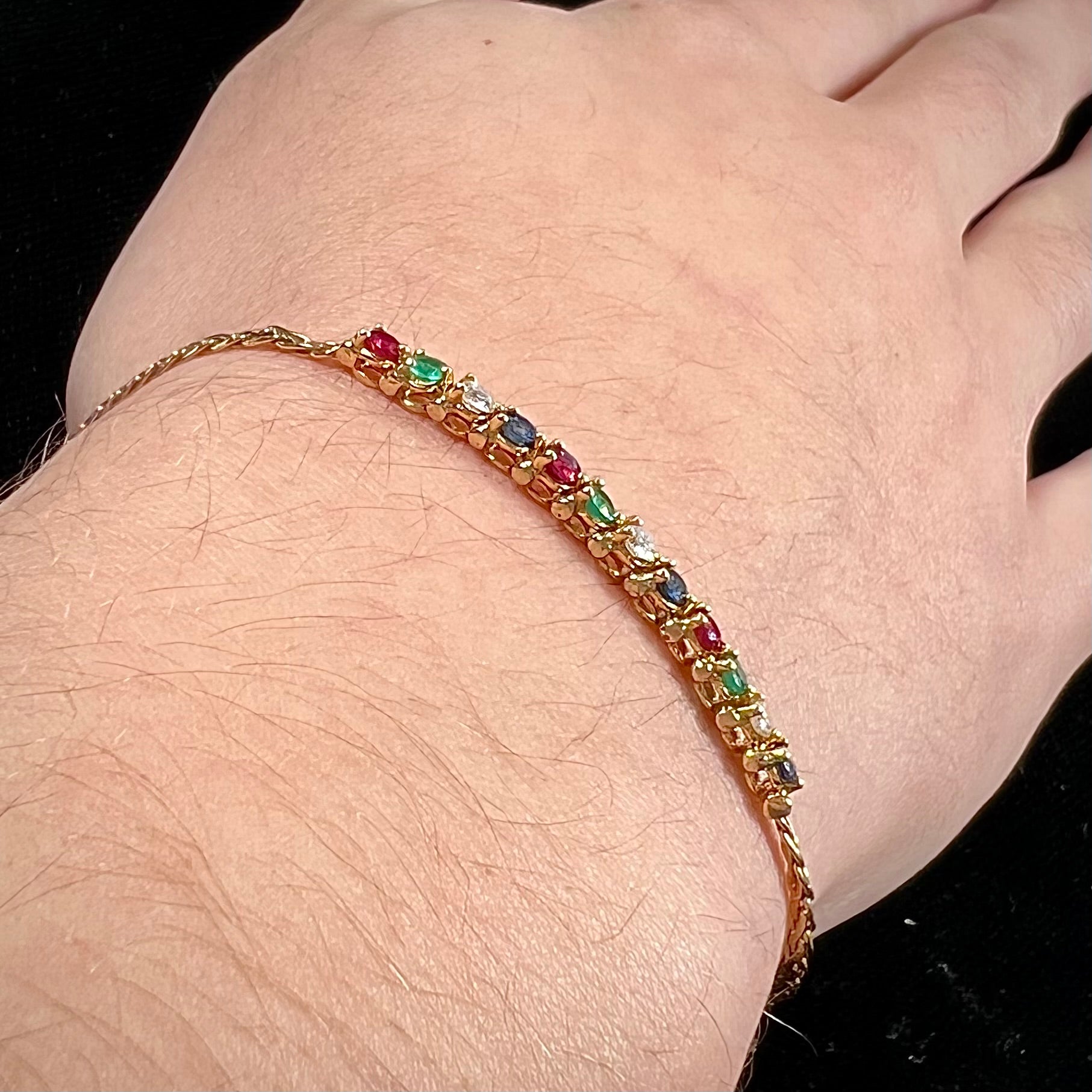 An 18k yellow gold bracelet set with natural rubies, sapphires, diamonds, and emeralds.