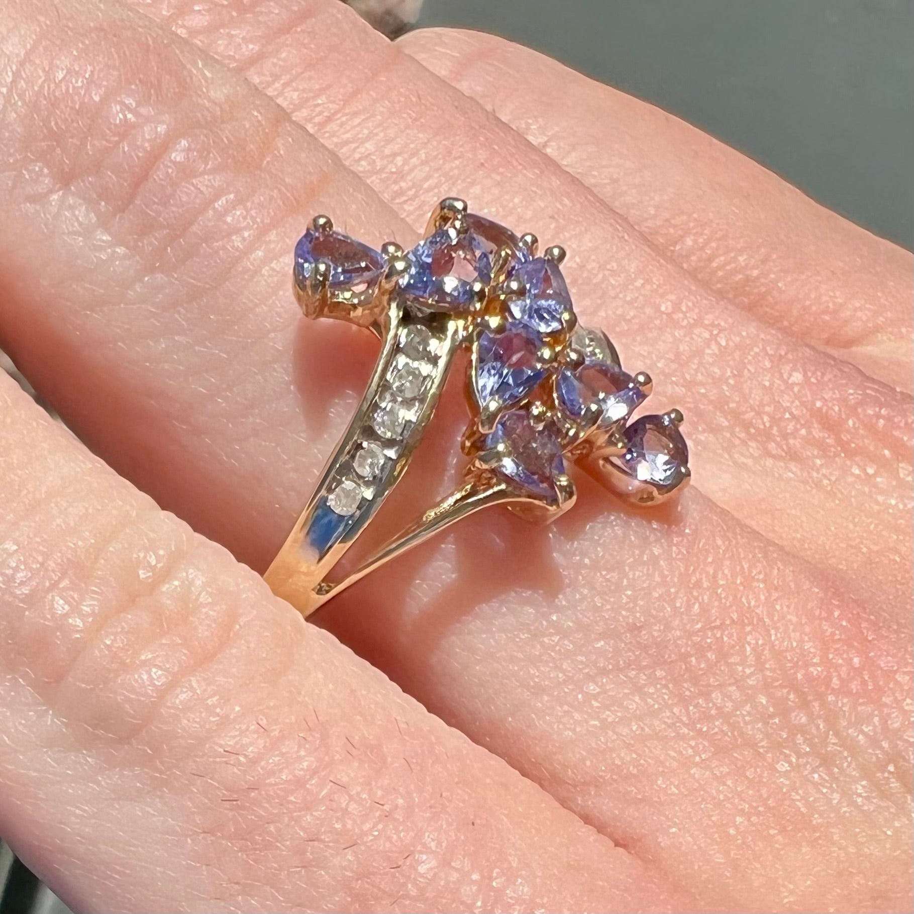 A pear shape tanzanite cluster ring channel set with diamonds in yellow gold.